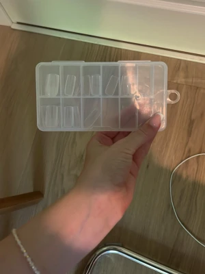 Transparenta press-on naglar i ask - Säljer ett set med transparenta press-on naglar i olika storlekar. Naglarna har en rak, fyrkantig form och kommer i en praktisk plastask med fack för enkel förvaring och sortering. Perfekt för dig som vill fixa snygga naglar snabbt hemma.
