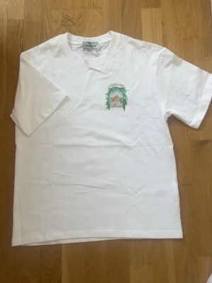 Vit Casablanca t-shirt med tryck - Vit t-shirt från Casablanca med färgglatt tryck på ryggen och mindre tryck på bröstet. Klassisk passform och rund hals. Perfekt för dig som gillar stilrena plagg med en twist. Materialet är mjuk bomull.