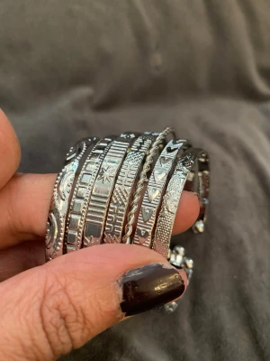 Set med silverfärgade armband - Säljer ett set med sju silverfärgade armband i olika mönster och former. Armbanden har graverade detaljer som stjärnor, hjärtan, geometriska former och tvinnad design. Perfekta för att mixa och matcha för en personlig stil.