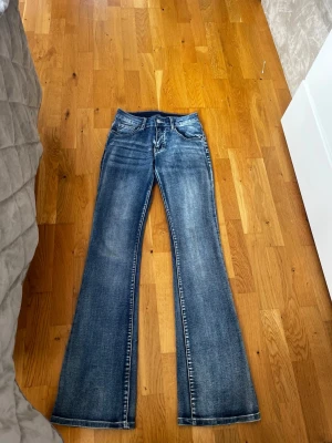 Blå bootcut jeans med slitningar - Säljer ett par blå bootcut jeans med snygga slitningar och tvättade detaljer. Jeansen har klassisk femficksmodell, normal midja och utsvängda ben. Perfekta för dig som gillar en retro och avslappnad stil.