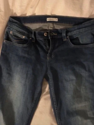 MörkBlå bootcut jeans med slitningar - Säljer ett par klassiska blå bootcut jeans med snygga slitningar och fem fickor. Jeansen har normal midja och är tillverkade i denim med lätt stretch för skön passform. Perfekta för en avslappnad och trendig look. Det är storlek L men den sitter som M