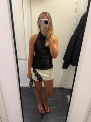 Vit kortkjol med svart spetsdetalj - Säljer en vit kortkjol med snygg svart spetsdetalj längs ena sidan. Kjolen har en rak passform och är perfekt för dig som vill ha en trendig och stilren look. Materialet känns mjukt och lätt, vilket gör den skön att bära under varma dagar.
