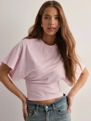 Nelly (pink) - Säljer en ljusrosa croppad topp med rund hals och vida, korta ärmar. Toppen har en tight passform i midjan och är gjord i mjuk bomull. Perfekt att styla med jeans eller kjol för en trendig look.