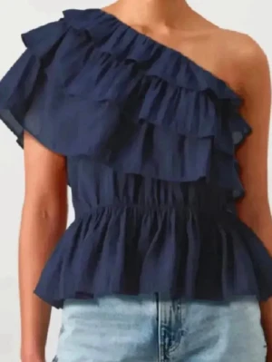  volangtopp - SÖKER!!!Snygg marinblå topp med volanger och oneshoulder-design. Toppen har en elastisk midja som ger en feminin siluett och är perfekt för dig som vill sticka ut lite extra. Passar till både jeans och kjol för en trendig look.