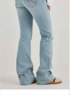 nelly jeans  - Säljer ett par ljusblå bootcut jeans med snyggt broderi på bakfickan. Jeansen har en klassisk femficksmodell och är tillverkade i denim med lätt stretch. Perfekta för dig som gillar en avslappnad men trendig stil.