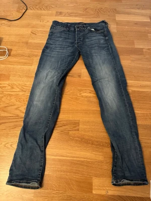 Blå slim fit jeans från Jack & Jones - Snygga blå slim fit jeans från Jack & Jones, modell Glenn. Jeansen har klassisk femficksdesign, normalhög midja och lätt slitna detaljer framtill för en avslappnad look. Perfekta för dig som gillar en smalare passform. 31 32 storlek