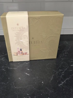 Rituals Intuitia giftset - Obs innan köp! Den guldfärgade gummisnodden saknas och lådan har smärre skönhetsfel. Allt är oanvänt!Snygg presentbox från Rituals i serien Intuita. Lådan är beige med gulddetaljer och innehåller flera skönhetsprodukter som duschskum, kroppskräm och handtvål. Perfekt som gåva till någon som gillar lyxiga hudvårdsprodukter.