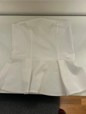 Vit  tubtopp  - Säljer en stilren vit  tubtopp i storlek XS. Toppen har en lätt utsvängd nederdel som ger en snygg siluett och är perfekt för att skapa en clean och trendig look. Materialet känns mjukt och bekvämt mot huden. Endast använd en gång super bra skick 