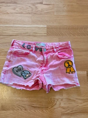Rosa shorts med patches och fransar Zara strl 152 - Säljer ett par ljusrosa shorts med coola patches som diamant, hjärta och rosett. Jätte fina från Zara strl 152