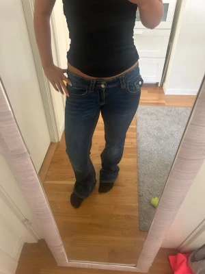 Mörkblå bootcut jeans med låg midja - Säljer ett par mörkblå bootcut jeans med låg midja och dubbla knappar fram. Jeansen har klassiska fickor både fram och bak samt kontrastsömmar. Perfekta för dig som gillar en avslappnad men ändå trendig look. Midjemått 35, innerbensmåttet 75