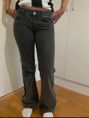 Svarta bootcut jeans med fickdetalj - Säljer ett par svarta bootcut jeans med snygg knappdetalj på bakfickan. Jeansen har klassisk femficksdesign och är tillverkade i ett mjukt denimtyg med lätt tvättad look. Perfekta för dig som gillar en avslappnad men trendig stil.