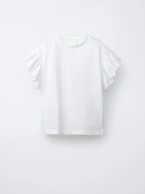 Vit topp med volangärmar från Zara - Snygg vit topp från Zara med rund halsringning och korta volangärmar som ger en trendig touch. Tillverkad i mjuk bomull som känns skön mot huden. Perfekt att styla med jeans eller kjol för en fräsch look.