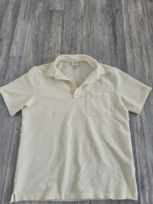 Vit kortärmad skjorta från H&M - Kortärmad beige skjorta från H&M i regular fit. Skjortan har en mjuk, strukturerad bomullskänsla och en bröstficka. Perfekt till sommaren/sensommaren med sin luftiga design och klassiska krage.