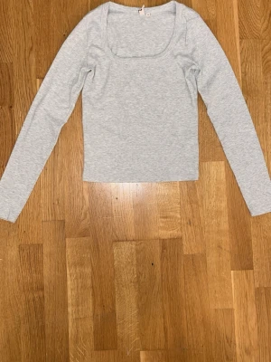 Ljusgrå långärmad topp - En enkel och stilren ljusgrå långärmad topp med rundad urringning. Toppen är croppad och har en mjuk, stretchig känsla som passar perfekt till jeans eller kjol. Perfekt basplagg för din garderob.
