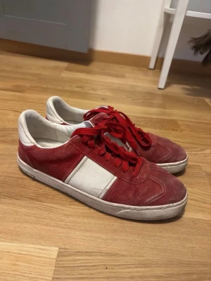 Valentino flycrews - Snygga sneakers i rött och vitt med klassisk låg profil och röda skosnören. Ovandelen är i mockaliknande material och detaljer i vitt läder. Yttersulan är svart med vågigt mönster undertill. Perfekta för en avslappnad och trendig look.