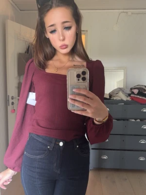 Vinröd topp med puffärmar - Trendig vinröd topp med fyrkantig ringning och långa puffärmar. Toppen är croppad och har en ribbad struktur som ger en snygg passform. Perfekt att styla med höga jeans för en cool look.