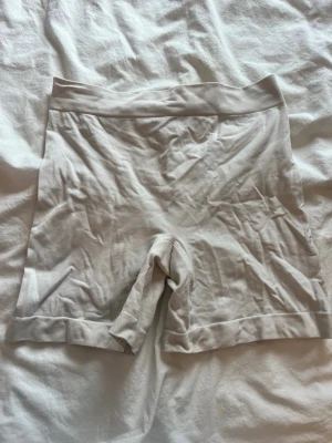 Vita cykelshorts från Kappahl - Säljer ett par vita shapewear-shorts från Kappahl i storlek S. De är tillverkade i ett stretchigt material med 92% polyamid och 8% elastan. Shortsen har hög midja och slät, sömlös design som formar och ger stöd under kläder. Använder inte dom så det är därför jag säljer dom 