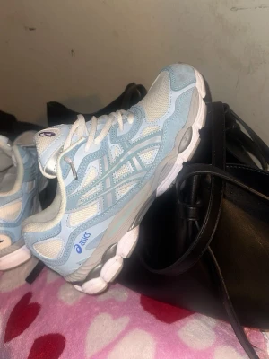 Asics ljusblå och vita sneakers - Säljer ett par fräscha Asics sneakers i ljusblått och vitt. Skorna har meshpaneler för bra ventilation, klassisk Asics-logga på sidan och en chunky vit sula med grå detaljer. Perfekta för dig som gillar sportig och trendig stil.