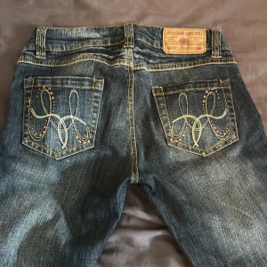 Blå utsvängda jeans med broderade bakfickor - Snygga blå jeans från Jessy Logan med coola broderier och nitar på bakfickorna. Jeansen har klassisk femficksdesign, kontrastsömmar och en lätt tvättad look.                                                               Jag är 170 cm och de är lite korta på mig💗