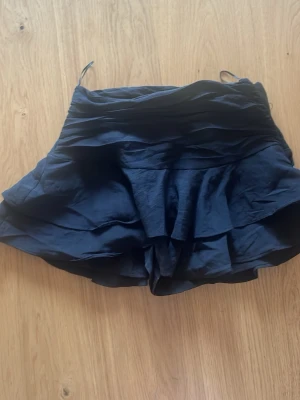 Svart volangskort kjolshorts - Supersnygga svarta skorts med volanger och hög midja. Kjolshortsen har en flowy passform prislappen fortfarande kvar. 