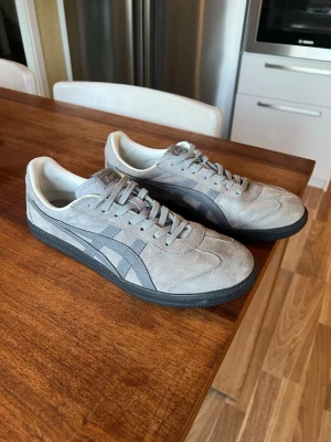 Onitsuka Tiger – Grå mocka (stl 42,5) - Säljer ett par riktigt snygga och klassiska sneakers från Onitsuka Tiger i grå mocka med mörkgrå detaljer. En tidlös modell som passar till det mesta.  Storlek: 42,5 (UK 8 / 27 cm) Skick: Mycket gott skick – använda fåtal gånger. Fräscha både invändigt och i sulan (se bilder). Material: Ovandel i mjuk mocka.  Skickas med spårbar frakt, och jag skickar antingen samma dag eller dagen efter betalning. Först till kvarn!