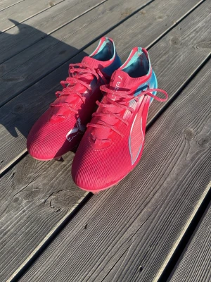 Helt Nya Puma fotbollsskor - Säljer ett par helt nya fotbollsskor från Puma i en cool rosa och blå färgkombination. Skorna har snörning, låg profil och en lätt ovandel med Pumas logga på sidan. Perfekta för dig som vill sticka ut på planen och få bra grepp i spelet.