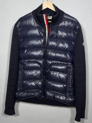 Maglione Tricot Cardigan - Mörkblå hybridjacka från Moncler. Dragkedjan har 2 olika lägen för att antingen visa franska flaggen längs zip eller inte. Väldigt sällsynt och eftertraktad modell. Jackan är i fint skick med endast lite små flaws på en av armarna, kontakta för bilder. Storlek L, men då Moncler är något små i storlekarna skulle jag säga att denna passar en Medium bättre. Äkthetsintyg finns och massvis av referenser att visa upp!