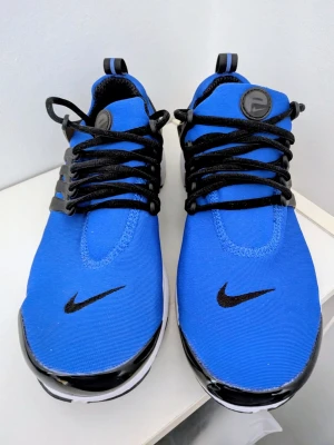 Blå Nike Presto  sneakers med svart swoosh - Snygga blå sneakers från Nike Presto med svart swoosh på tån och svart snörning. Skorna har en vit och svart sula samt detaljer i plast vid snörningen. Ovandelen är i textil för en sportig look.
