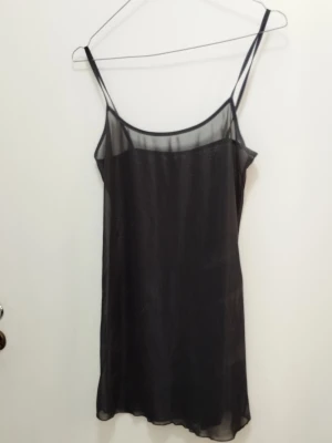 Svart transparent mesh klänning / underklänning - Säljer en svart, tunn och transparent klänning i meshmaterial. Klänningen har smala axelband och rak passform. Perfekt att använda som lager-på-lager-plagg, t.ex. över ett linne eller bikini. Funkar även som underklänning Materialet är stretchigt, mjuk och följsamt, vilket syns på närbilden där handen syns tydligt genom tyget. Bredd i bysten ca 80cm, länge ca 75cm.