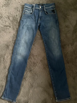 Blå slim fit jeans med slitningar - Snygga blå slim fit jeans med lätt slitna detaljer och klassiska fem fickor. Jeansen har en smal passform och kontrastsömmar. Perfekta för en avslappnad och trendig look. Materialet är denim i bomull.