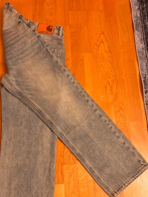 Ljusblå raka jeans från Carhartt (aldrig använda! Pris kan diskuteras!) - Säljer ett par ljusblå jeans från Carhartt med rak passform och klassisk femficksdesign. Jeansen har en snygg vintage tvätt och ett brunt Carhartt-märke på bakfickan. Perfekta för en avslappnad och trendig look.