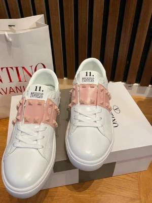 Valentino Rockstud Untitled sneakers - Snygga vita sneakers från Valentino med rosa band och ikoniska nitar över vristen. Skorna har en klassisk låg profil, snörning och detaljer i skinn. Perfekta för dig som vill sticka ut med en lyxig touch och cool design. Pris går att diskutera 