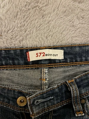 Levis Bootcut jeans 572 - Säljer ett par vintage lågmidjade bootcut jeans, modell 572 från Levis. Jeansen har en snygg tvätt med lätt slitningar och kontrastsömmar. Perfekta för dig som gillar retrovibbar. Storlek 30x34 ~ 36
