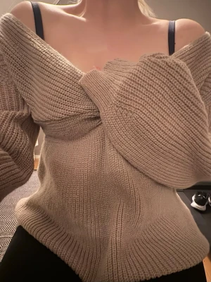 Oanvänd Beige stickad tröja med twist - Säljer en oanvänd beige stickad tröja med snygg twistdetalj framtill och djup v-ringning. Tröjan har långa ärmar och är gjord i ett mjukt, ribbstickat material.