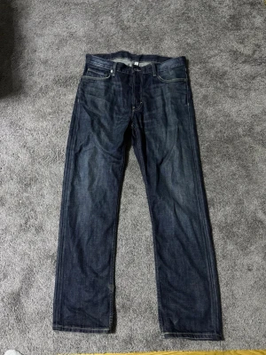Weekday klean jeans - Säljer ett par mörkblå jeans med rak passform och klassisk femficksdesign. Jeansen har en snygg tvätt med subtila slitningar och är tillverkade i denim. Perfekta för en avslappnad och stilren look.