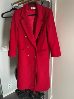 Röd dubbelknäppt vintage kappa med guldknappar - Stilren röd vintage kappa med dubbelknäppning och dekorativa guldknappar. Klassisk krage och två fickor framtill.  - Original vintage från J.G. Hook och 100% bombull.  - Inga tecken av slitage, mycket fint skick.  - Passar Strl. M, lätt oversize för Strl. S.  - Rak form med axelvaddar, viss tyngd. - Guldknappar med fina detaljer.  Har varit hos kemtvätten inför försäljningen.