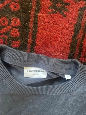 Mörkblå tröja från Lindbergh - En stilren mörkblå tröja från Lindbergh i relaxed fit. Tröjan har rund halsringning, långa ärmar och ribbade muddar vid hals, ärmslut och nederkant. Perfekt för dig som gillar enkel och klassisk stil.