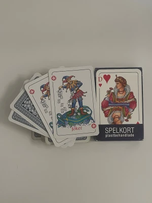 Kortlek plastbehandlade spelkort - En klassisk kortlek med plastbehandlade spelkort. Korten har traditionella motiv, inklusive joker och hjärter dam. Baksidan är blå med vitt mönster. Perfekt för poker, bridge eller andra kortspel.