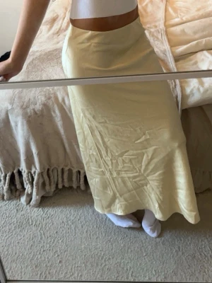 Ljusgul lång satinkjol från HM - Säljer en ljusgul lång kjol i satin-look med mjuk glans och enkel, rak passform. Aldrig använd. Kjolen har en clean midja utan synliga detaljer och faller snyggt längs benen. Perfekt för dig som gillar minimalistisk och stilren vibe.