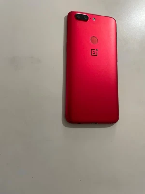 OnePlus 5T A5010 med 128 GB  android version 15 - This is an image of the OnePlus 5T smartphone in its limited edition red color. The phone is placed on a flat surface with its back facing up, showcasing the dual camera setup, fingerprint sensor, and the OnePlus logo.