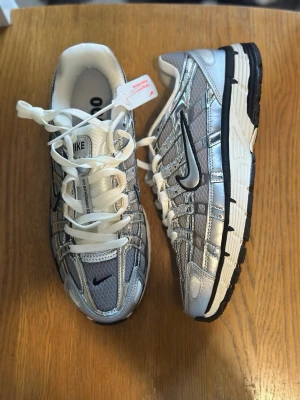 Nike p6000 metallic silver (Passar som EUR 40) - Snygga sneakers från Nike i silver och grått med svarta detaljer och vit sula. Skorna har en sportig design med mesh och syntetmaterial, samt klassisk Nike-logga på sidan. Perfekta för dig som gillar en futuristisk och trendig look.