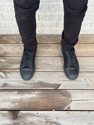 Svarta låga sneakers i mocka - Säljer ett par svarta sneakers med lågt skaft och klassisk design. Skorna har svarta skosnören, metallfärgade öljetter och ovandel i mocka. Yttersulan är svart och tån är förstärkt. Perfekta för en stilren och enkel look.