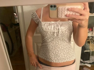 Vit blommig topp med rosett - Supersöt vit topp med små blommor och en söt rosett framtill. Toppen har korta puffärmar och en fin, feminin passform. Perfekt för dig som gillar romantisk stil och detaljer som spets och knytband.