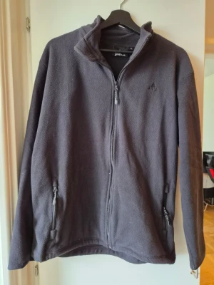 Svart fleecejacka Whistler S - Svart fleecejacka från Whistler med hög krage, hel dragkedja och två sidofickor med dragkedja. Jackan är enkel, mjuk och har en stilren look som funkar till många olika outfits.