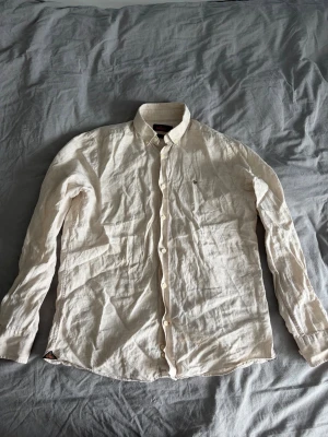 Beige linneskjorta med knappar - Säljer en stilren beige Morris skjorta i linne med klassisk krage och knäppning framtill. Skjortan har långa ärmar och en avslappnad passform, perfekt för varmare dagar. Enkel och tidlös design som passar till mycket.