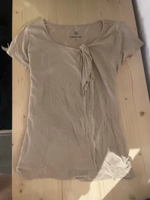 Beige topp med knyt fram - Säljer en beige topp med korta ärmar och rund halsringning. Toppen har en snygg knyt-detalj framtill. Perfekt till jeans eller kjol till skola/jobb. Pyttelitet hål framtill som lätt går att sy (se sista bild)😊💕