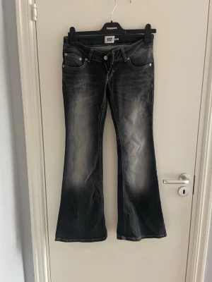 Svarta bootcut jeans med slitningar - Snygga svarta bootcut jeans med slitna detaljer och ljusare partier framtill. Klassisk femficksmodell med låg midja och utsvängda ben. Perfekta för en cool och avslappnad stil.