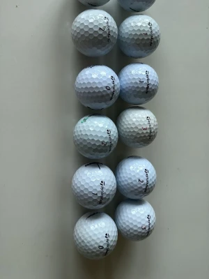 12 vita golfbollar TaylorMade - Säljer ett set med 12 vita golfbollar från TaylorMade. Bollarna har klassisk dimple-yta och märkning med siffror och TaylorMade-logga. Perfekta för dig som vill fylla på golfbagen inför säsongen. De är lite blandade bollar av märket TylorMade som är i mycket bra skick. 