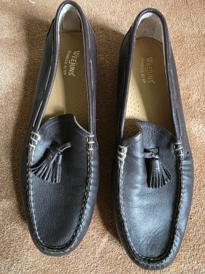 Bruna loafers med tofsar från Weejuns - Snygga mörkbruna loafers från Weejuns i äkta läder. Skorna har klassisk design med dekorativa tofsar framtill och kontrastsömmar runt tån. Perfekt för dig som gillar stilrena och tidlösa skor. Läderinnersula för extra komfort. Använda enstaka gång, i princip nyskick! 