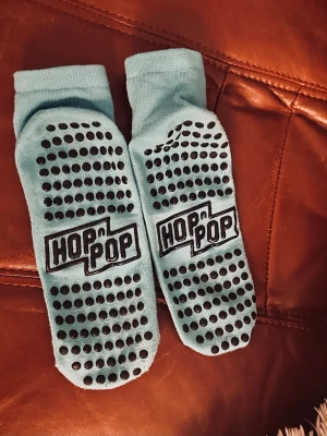Blå halksockor från Hop n Pop XL  - Säljer ett par ljusblå halksockor från Hop n Pop med svarta prickar undertill för extra grepp. Perfekta för trampolinpark eller inomhusaktiviteter. Mjukt material och stretchig passform. Logga på både ovansida och undersida.